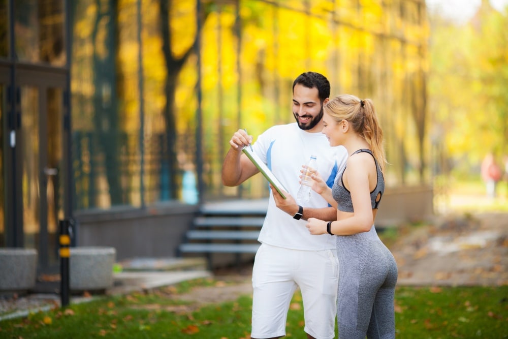 system motywacji pracowników - para młodych ludzi w stroju sportowym w parku czytająca plan treningowy